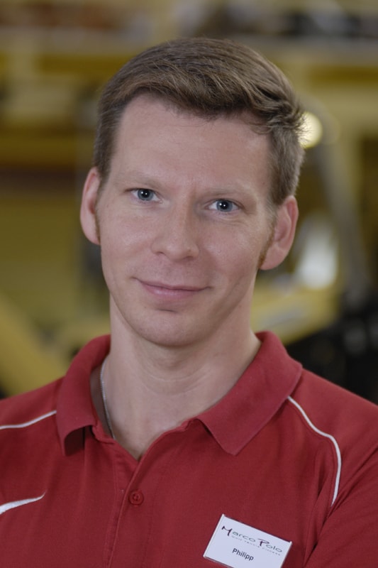 Fitnesstrainer Philipp trägt ein rotes Shirt und lächelt in die Kamera.
