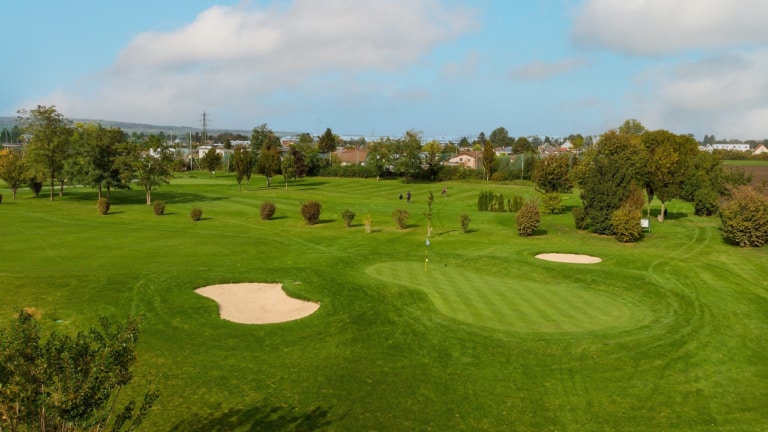 Überblick über ein Loch des Golfplatzes des Sportcenters Marco Polo, Wien im Hintergrund, zwei Golfspieler